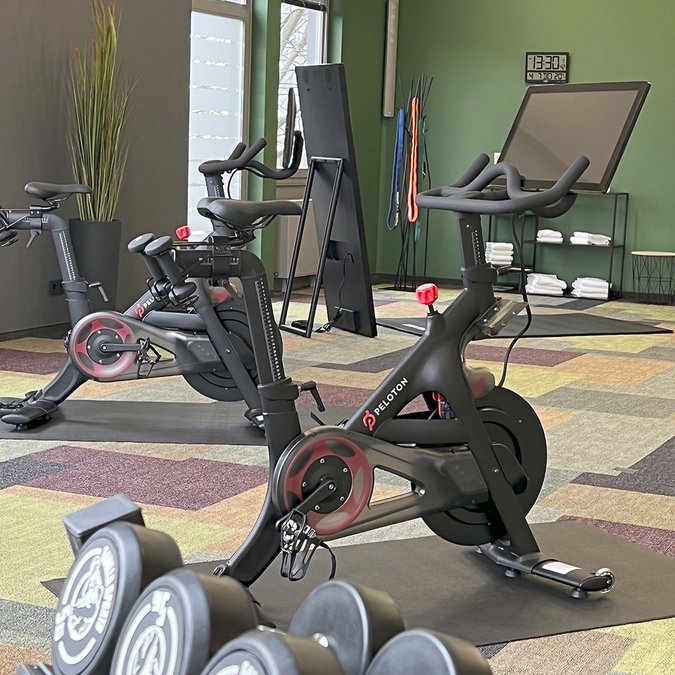 Unser Sauna- und Fitnessbereich Fitnessraum mit Peloton Bikes und Hanteln vor buntem Teppichboden