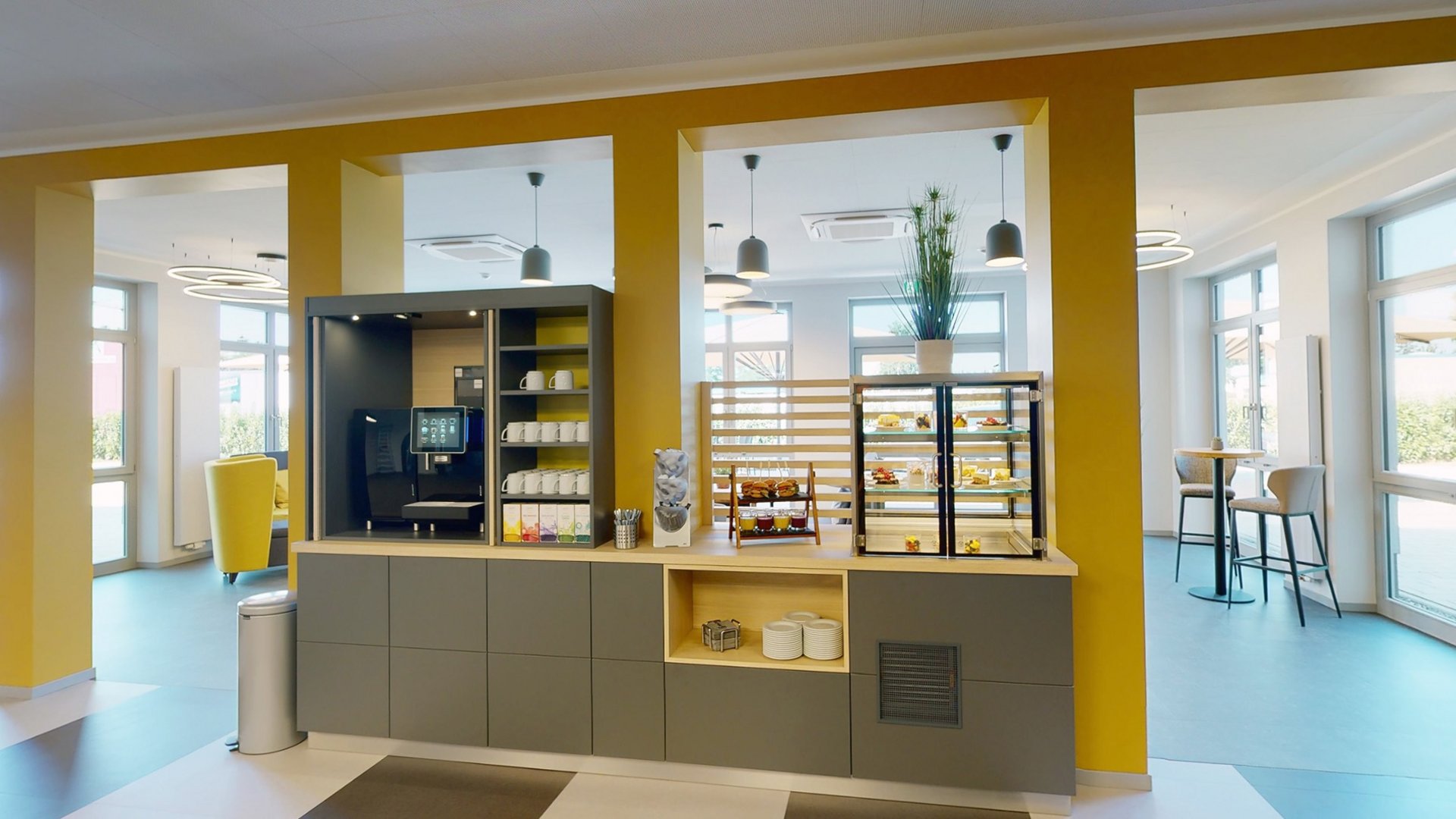 Ihr autarker und exklusiver Tagungsbereich: Ihr Hotel im Hotel Moderne Cafeteria mit Kaffeemaschine und Auslage für Snacks in hellem Raum