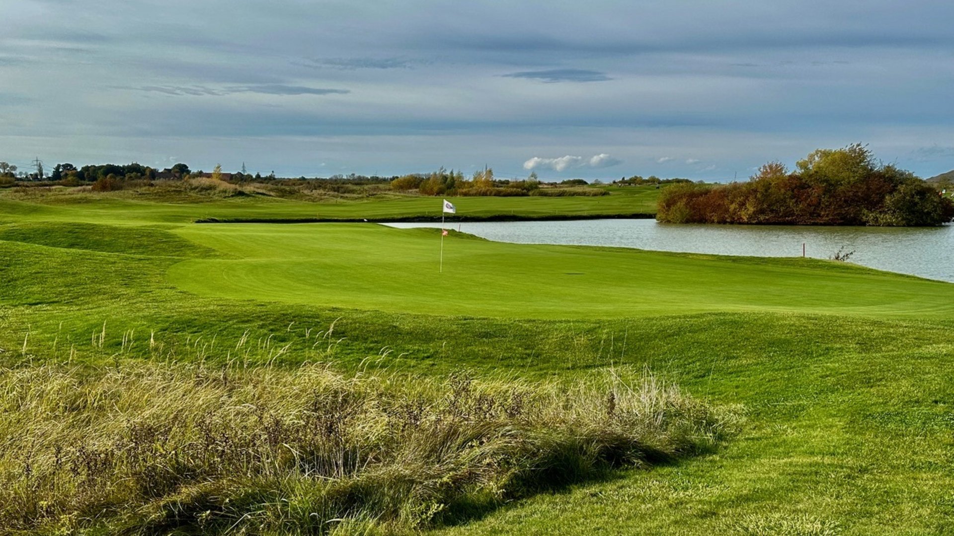 Golfwochenende inklusive Golfturnier Golfplatz mit Fahne am Grün neben einem Teich unter bewölktem Himmel