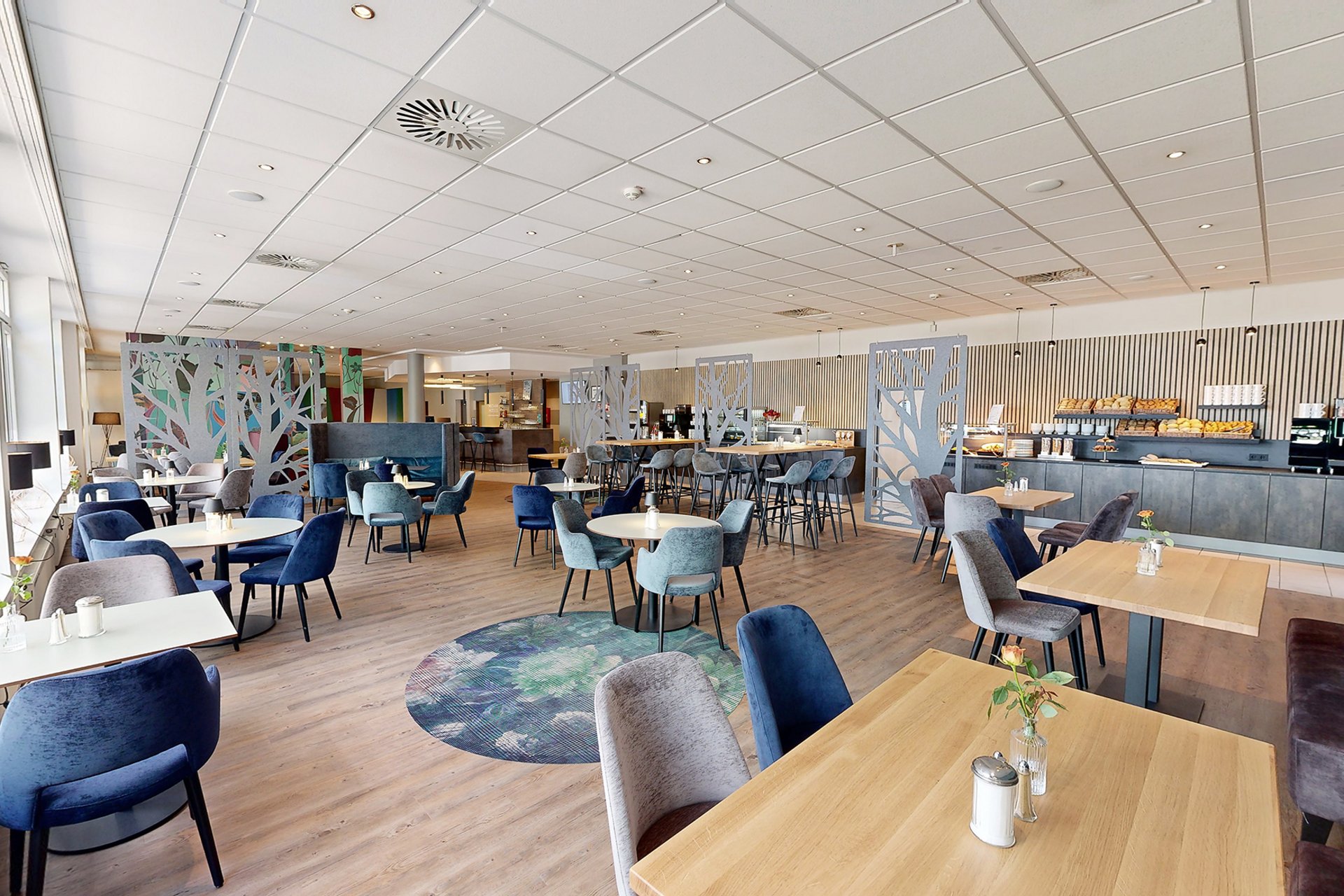 Unser Hotel an der Messe: die Bildergalerie Modernes Café mit Holzboden, blauen und grauen Stühlen und Buffet im Hintergrund