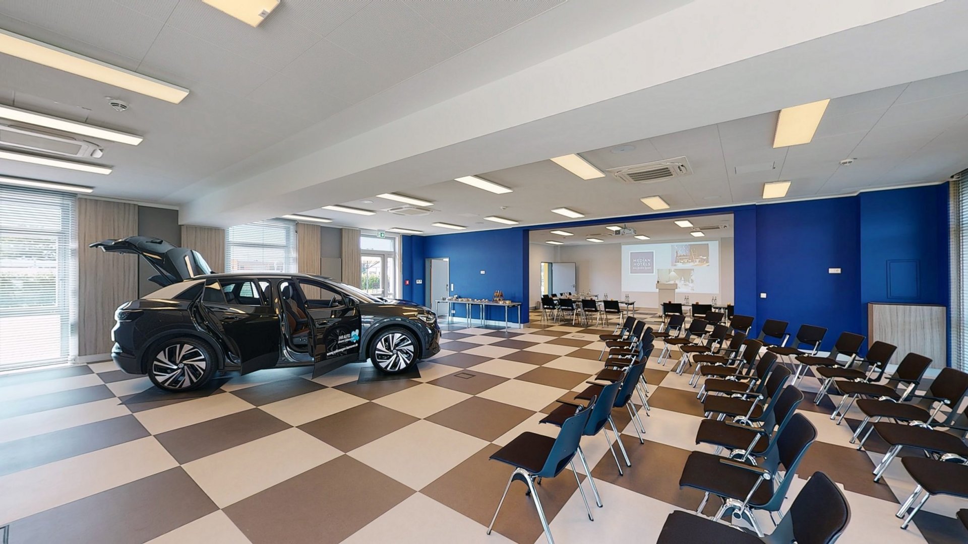 Ihr autarker und exklusiver Tagungsbereich: Ihr Hotel im Hotel Konferenzraum mit Stuhlreihen und einem schwarzen Auto mit offenen Türen
