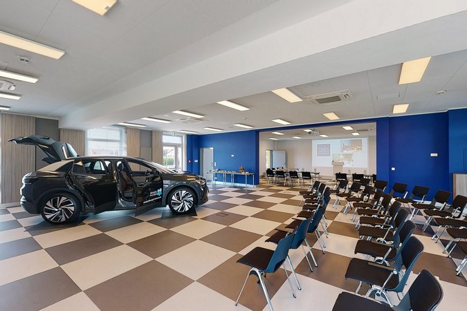 Hybrides Tagen in Lehrte Konferenzraum mit Stuhlreihen und einem schwarzen Auto mit offenen Türen