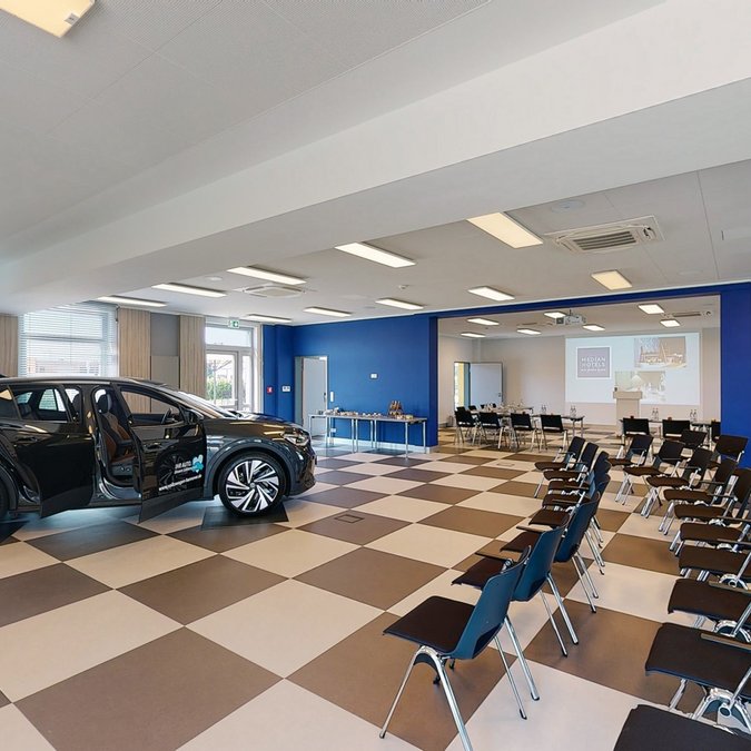 Ihr autarker und exklusiver Tagungsbereich: Ihr Hotel im Hotel Konferenzraum mit Stuhlreihen und einem schwarzen Auto mit offenen Türen