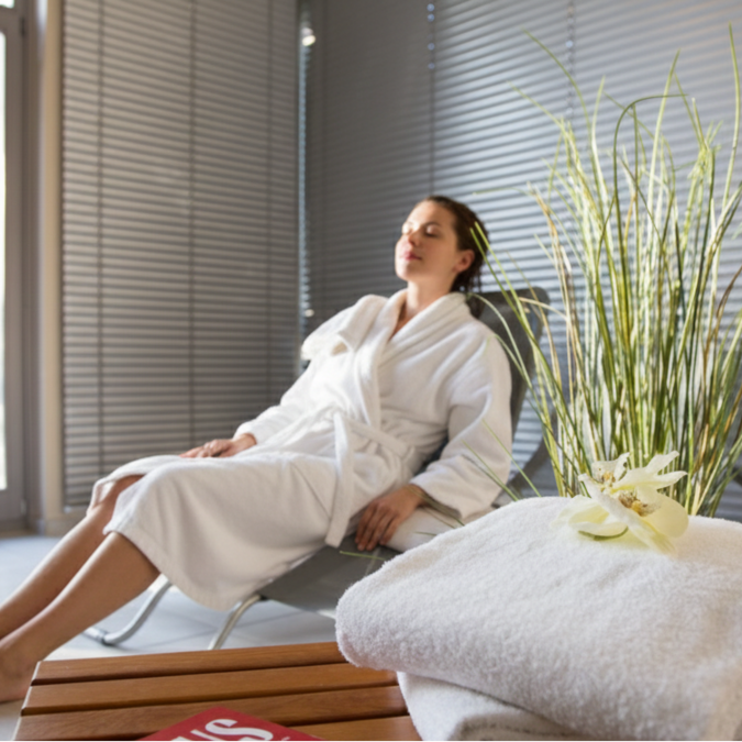 Unser Sauna- und Fitnessbereich Frau entspannt sich im weißen Bademantel auf Liegestuhl in hellem Raum