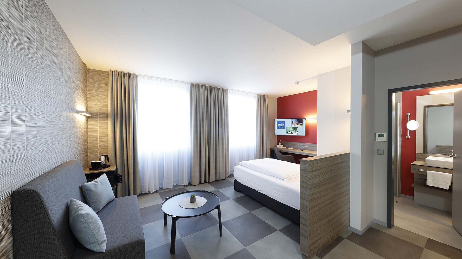 Ihr autarker und exklusiver Tagungsbereich: Ihr Hotel im Hotel Modernes Hotelzimmer mit Sofa, Bett und angrenzendem Bad