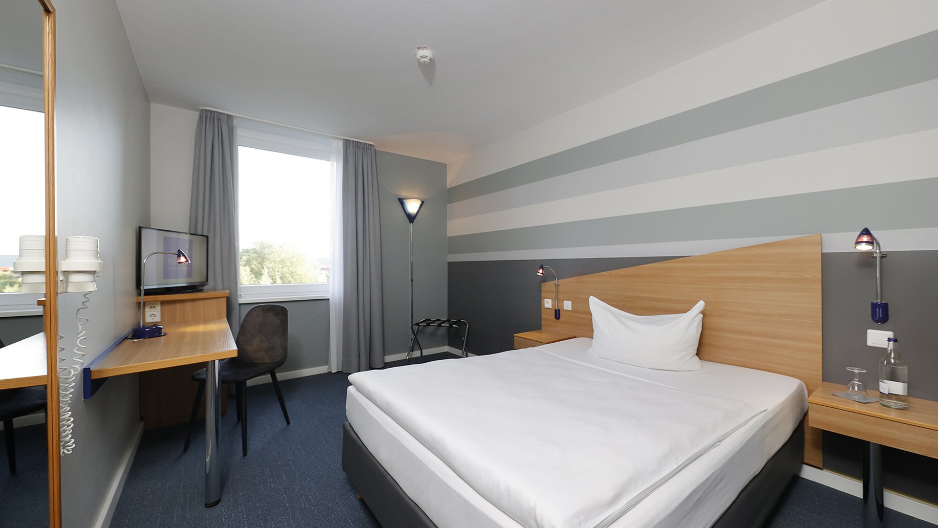Welcome to the Median Hotel Hannover Messe! Cozy hotel room with single bed, desk, and window with curtains