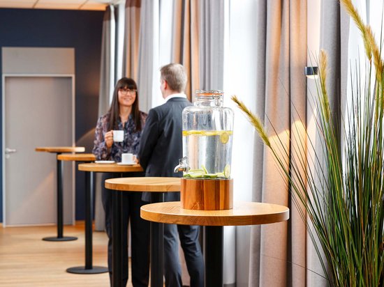 Median Hotel Messe Hannover – der Newsblog Glasbehälter mit Zitronenwasser und zwei Menschen im Gespräch im Hintergrund