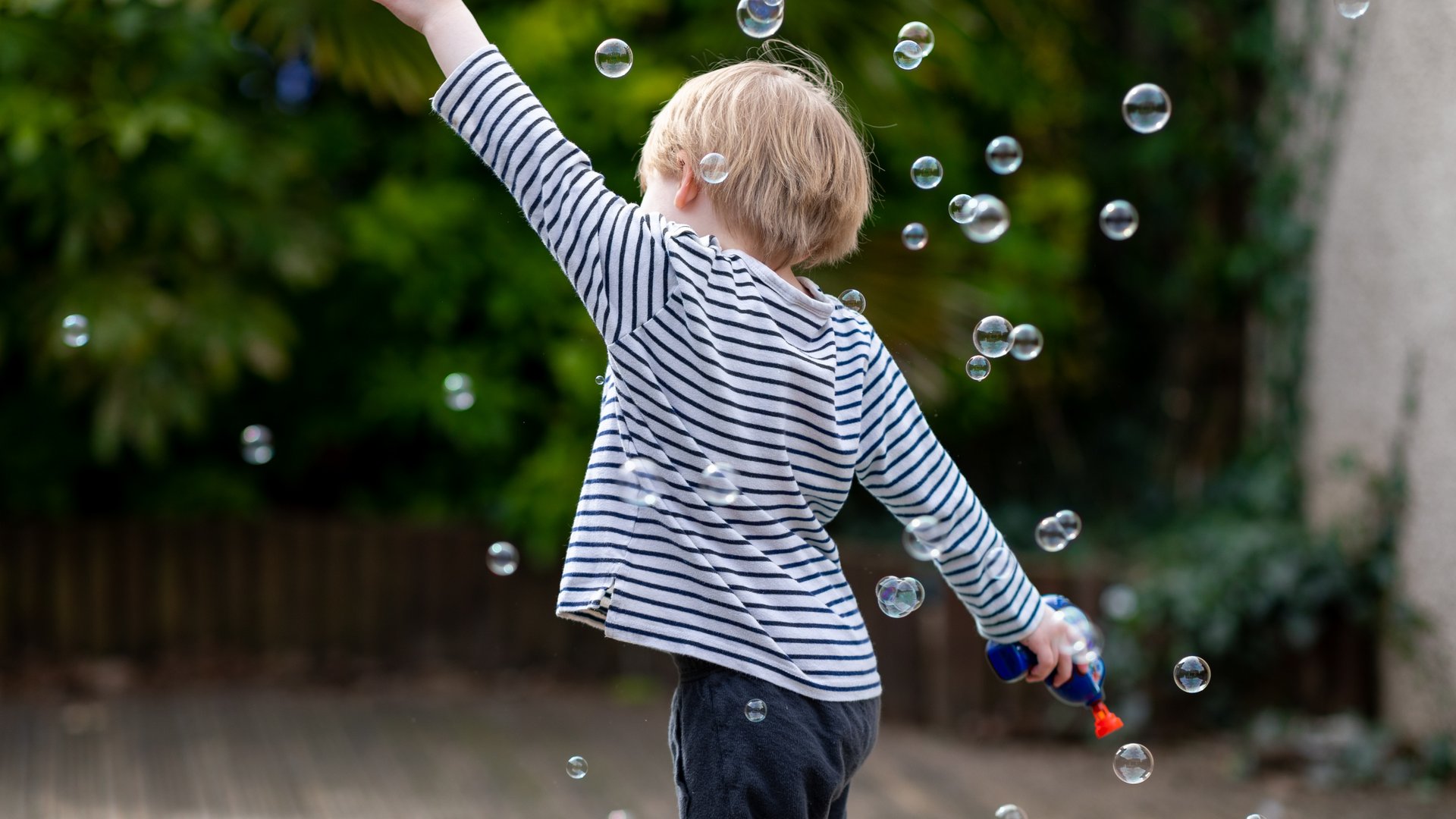 Die Messe für Luftsprünge Kind mit gestreiftem Shirt spielt mit Seifenblasen im Garten