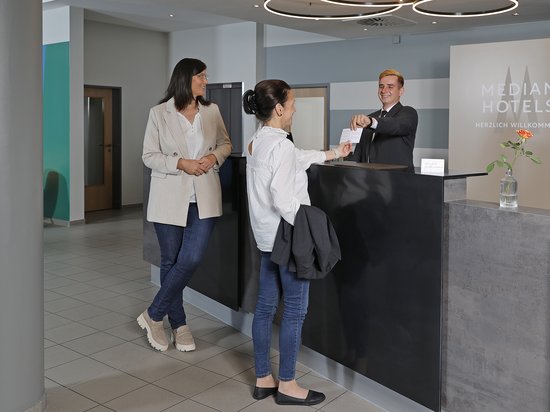 Median Hotel Messe Hannover – der Newsblog Zwei Frauen checken an der Hotelrezeption ein, Concierge übergibt Schlüsselkarte