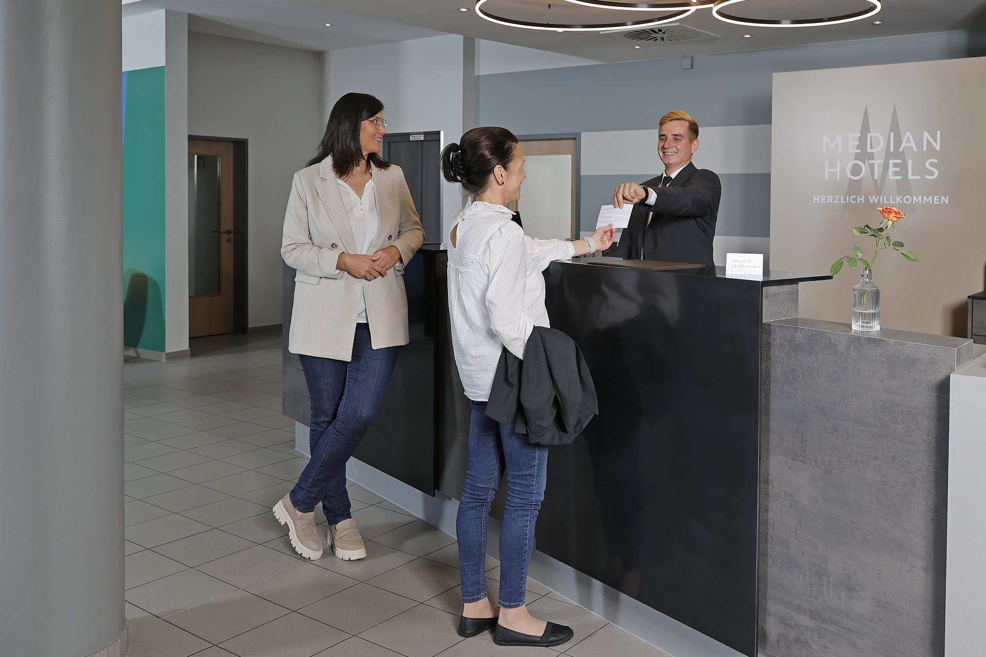 Unser Hotel an der Messe: die Bildergalerie Zwei Frauen checken an der Hotelrezeption ein, Concierge übergibt Schlüsselkarte