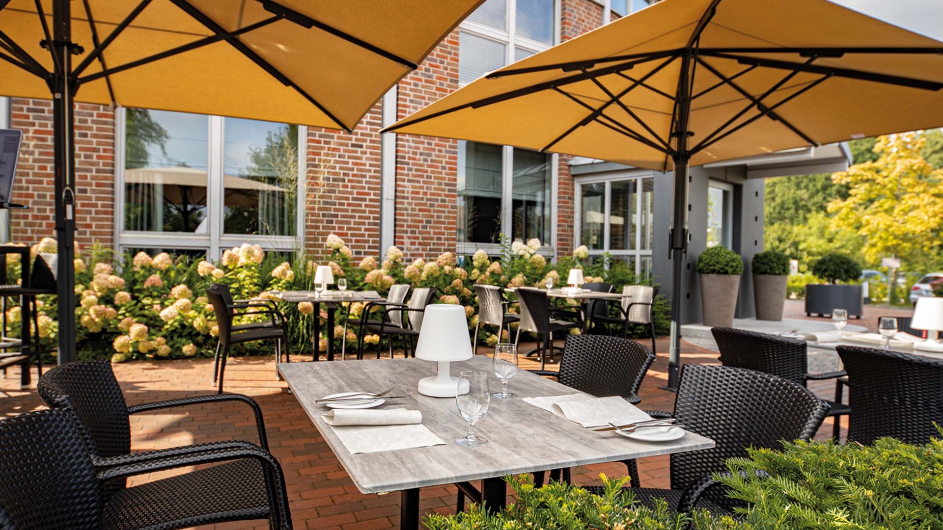Just outside Hanover: your restaurants in Lehrte Outdoor terrace with tables, chairs, and yellow umbrellas in front of brick building