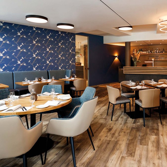 Viva – unser Hotel-Restaurant Modernes Restaurant mit blauem Vogel-Tapetenmuster und Holzboden
