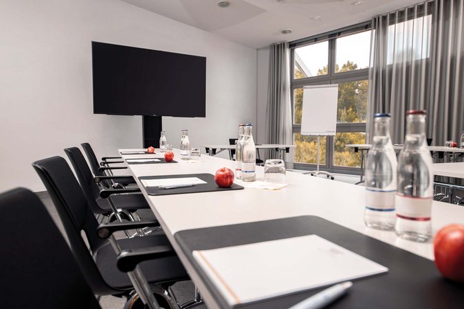 Ihr autarker und exklusiver Tagungsbereich: Ihr Hotel im Hotel Konferenzraum mit Tischen, Stühlen, Wasserflaschen, Äpfeln und Flipchart