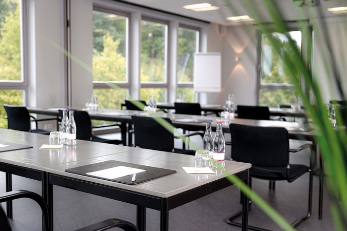 Ihr autarker und exklusiver Tagungsbereich: Ihr Hotel im Hotel Moderner Konferenzraum mit Tischen, Stühlen, Wasserflaschen und Notizblöcken