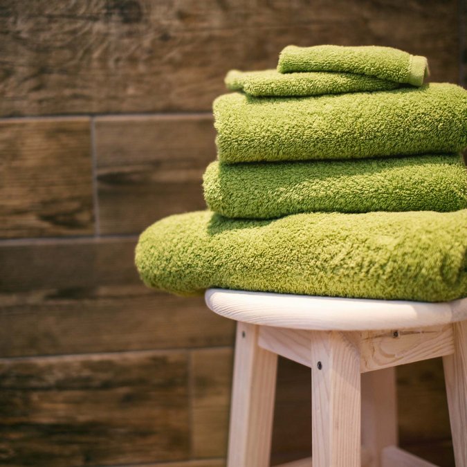 Our sauna and fitness area Stacked green towels on a stool in front of a wooden tile wall