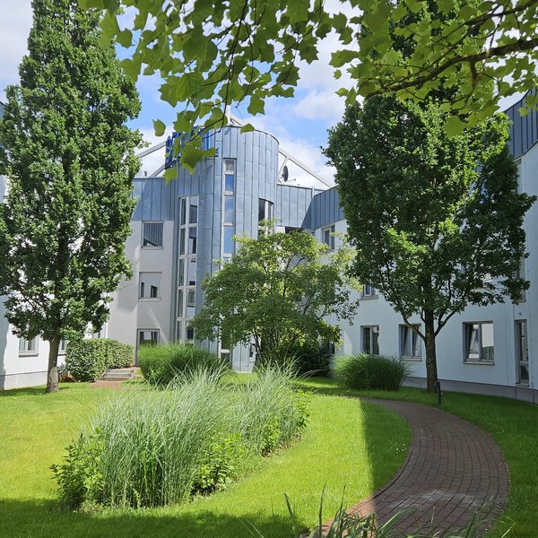 Median Hotel Hannover Lehrte Innenhof mit grünen Bäumen und Gebäuden umgeben bei Sonnenschein