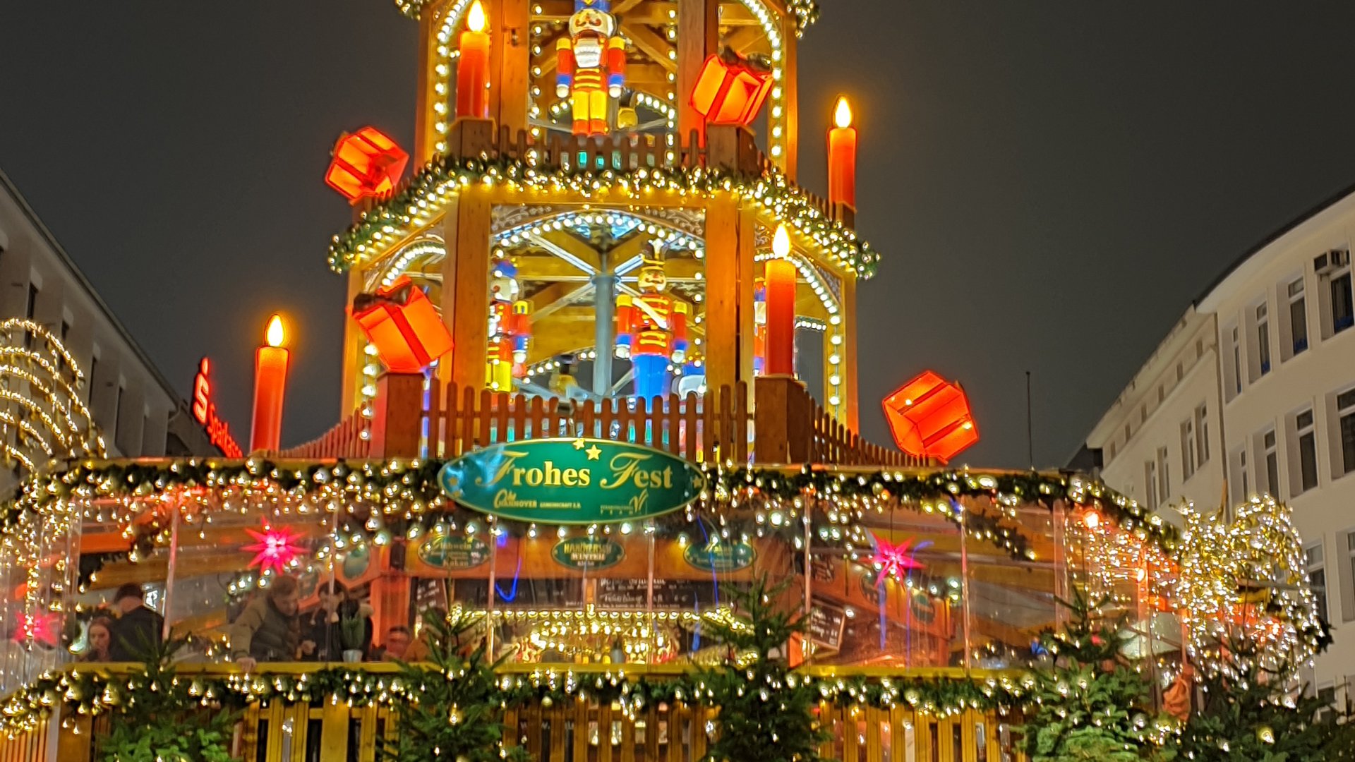 Weihnachtszauber ab 25.11.2025 Beleuchteter Weihnachtsmarktstand mit Pyramide und Menschen abends