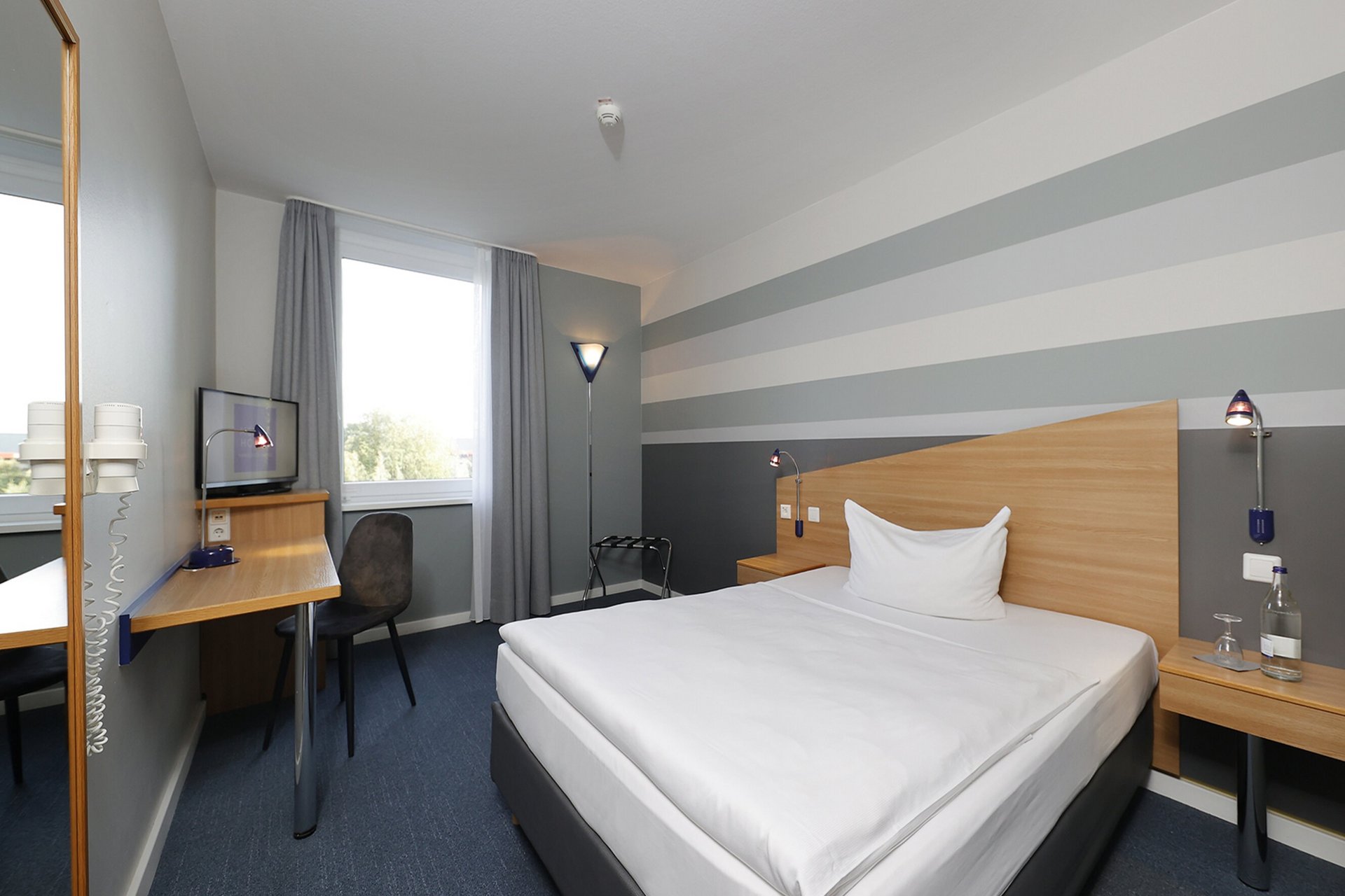 Our hotel at the exhibition centre: the picture gallery Modern hotel room with large bed, desk, and window with gray curtains