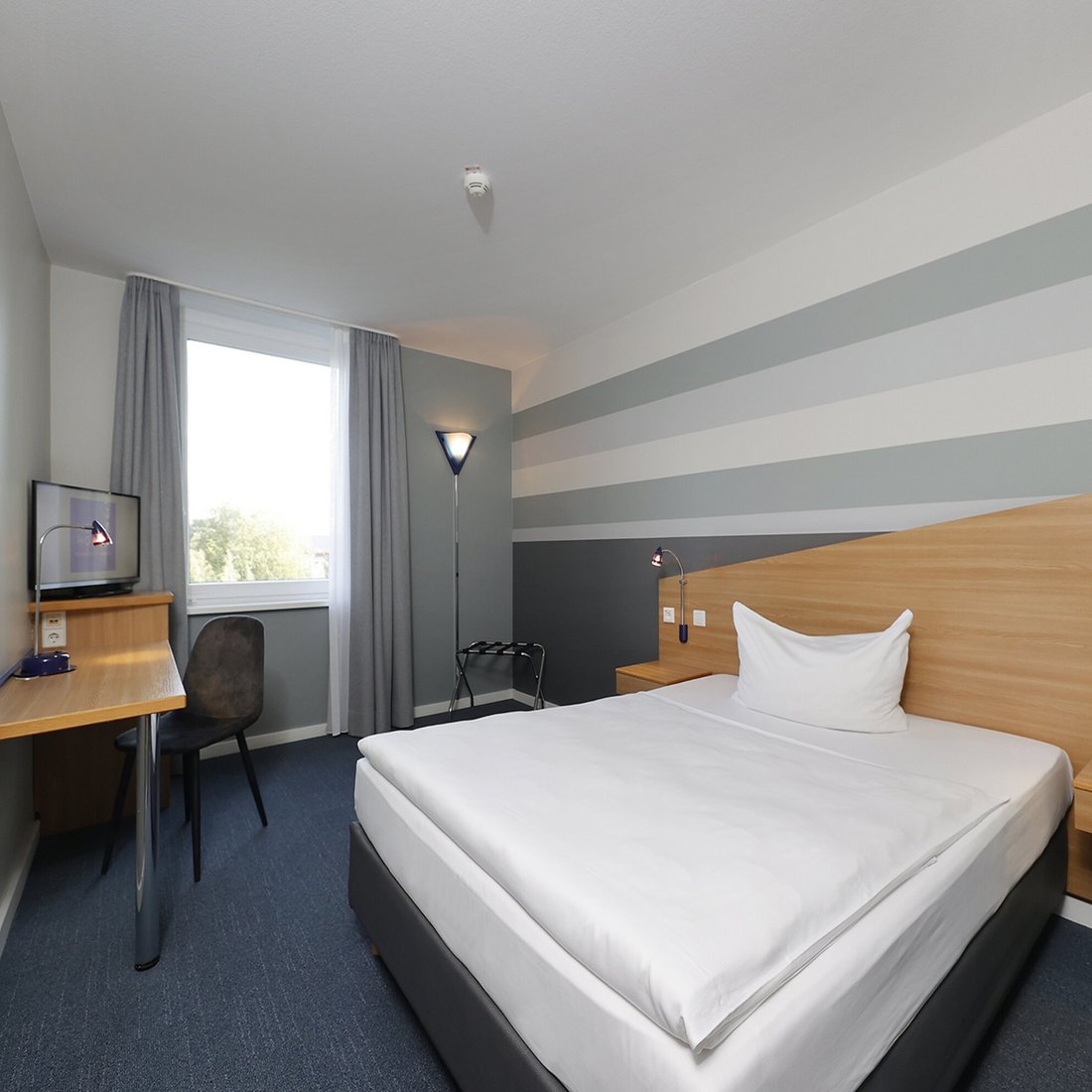 Ihr Hotel in Hannover: der Messe so nah Modernes Hotelzimmer mit großem Bett, Schreibtisch und Fenster mit grauen Vorhängen