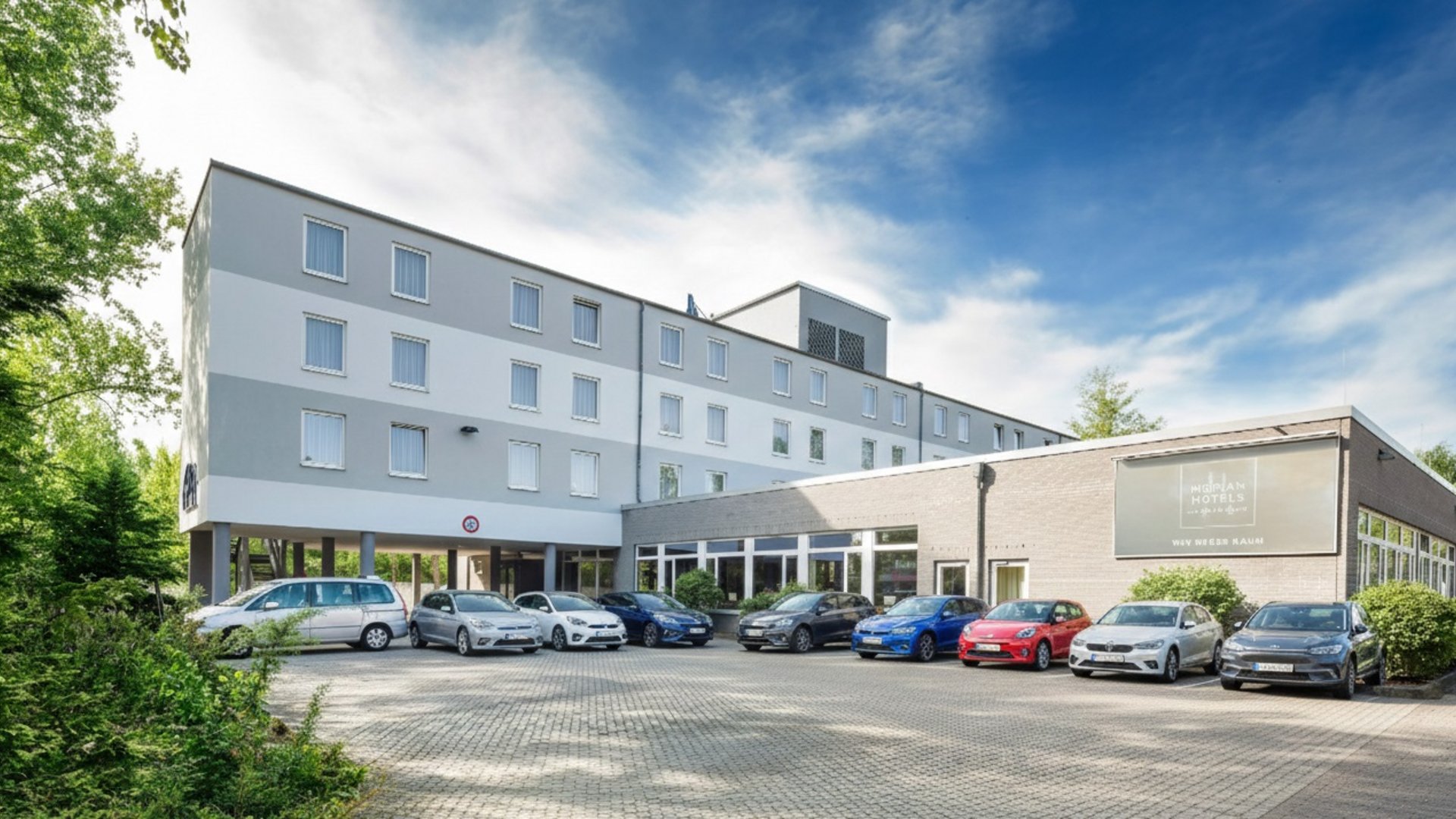 Welcome to the Median Hotel Hannover Messe! Front view of a hotel with parked cars and blue sky