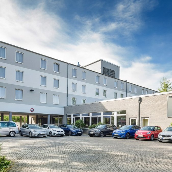 Ankommen - Parken - E-Auto laden Vorderansicht eines Hotels mit parkenden Autos und blauem Himmel
