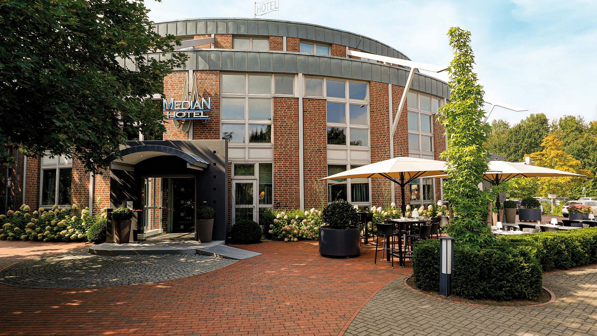 Median Hotel Hannover Lehrte Entrance of the Median Hotel with outdoor seating and umbrellas