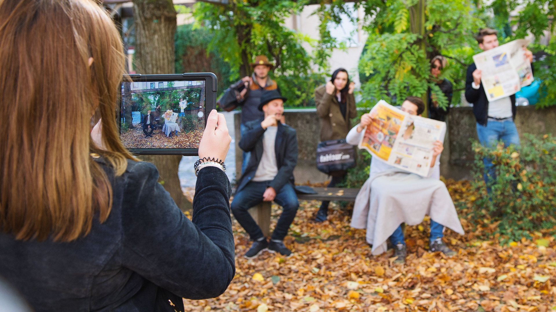 Teambuilding in Hannover und Umgebung Frau macht Foto von fünf Menschen im Park mit Zeitungen und Herbstlaub