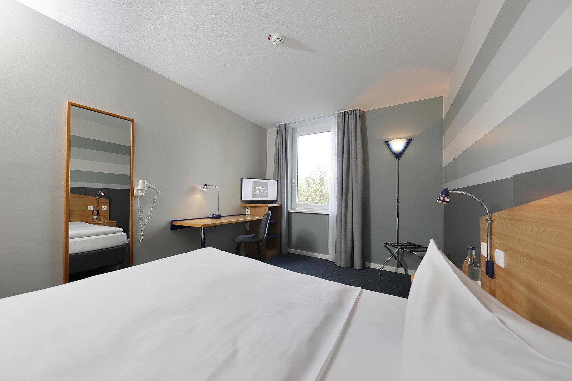 Unser Hotel an der Messe: die Bildergalerie Modernes Hotelzimmer mit Bett, Schreibtisch und großem Spiegel